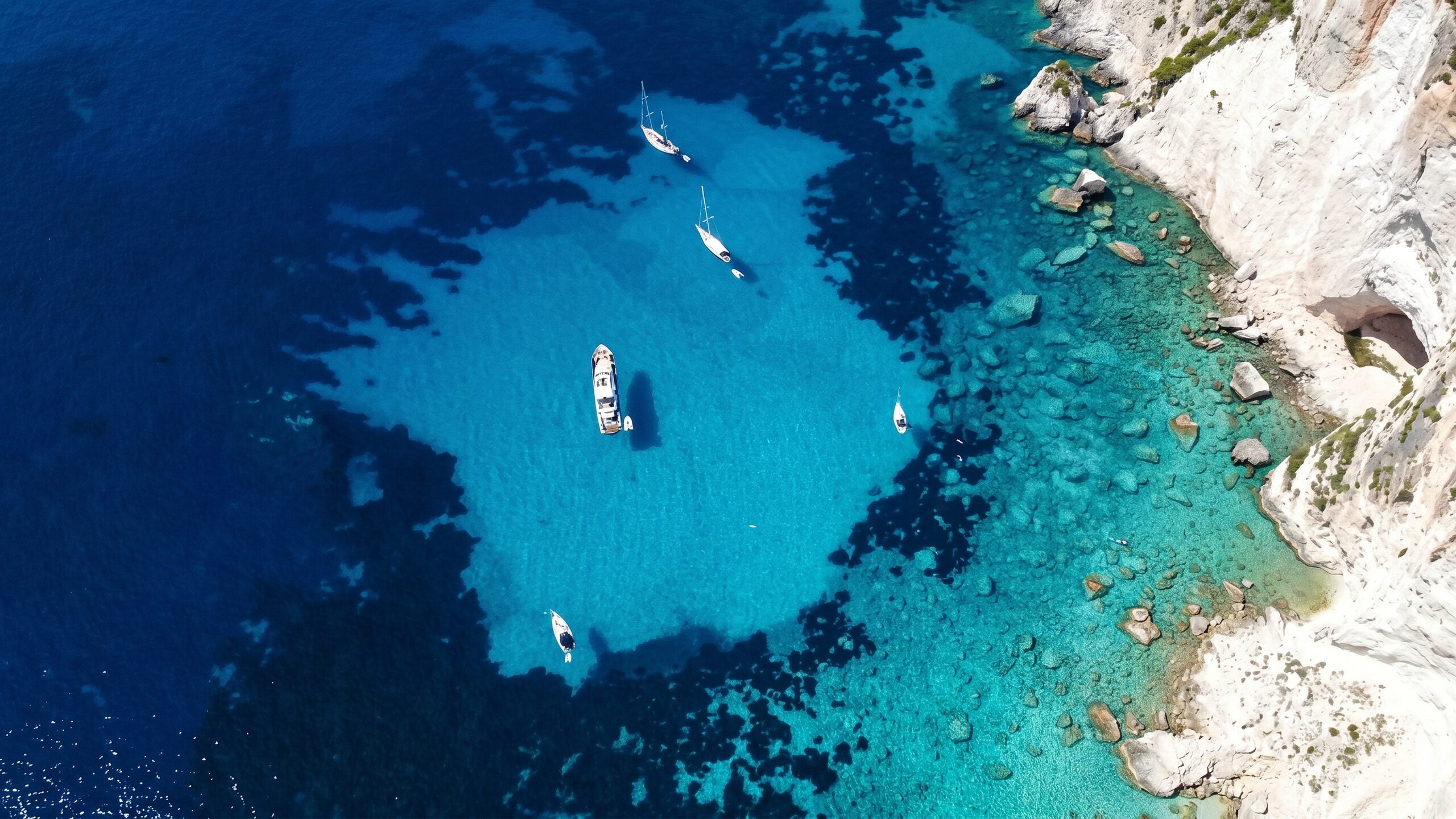 Yachts at anchor in a turquoise Aegean cove beneath white cliffs